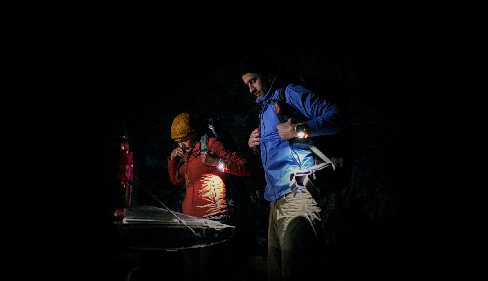Twee personen staan met lichtgevende horloges om in het donker en kijken naar beneden.