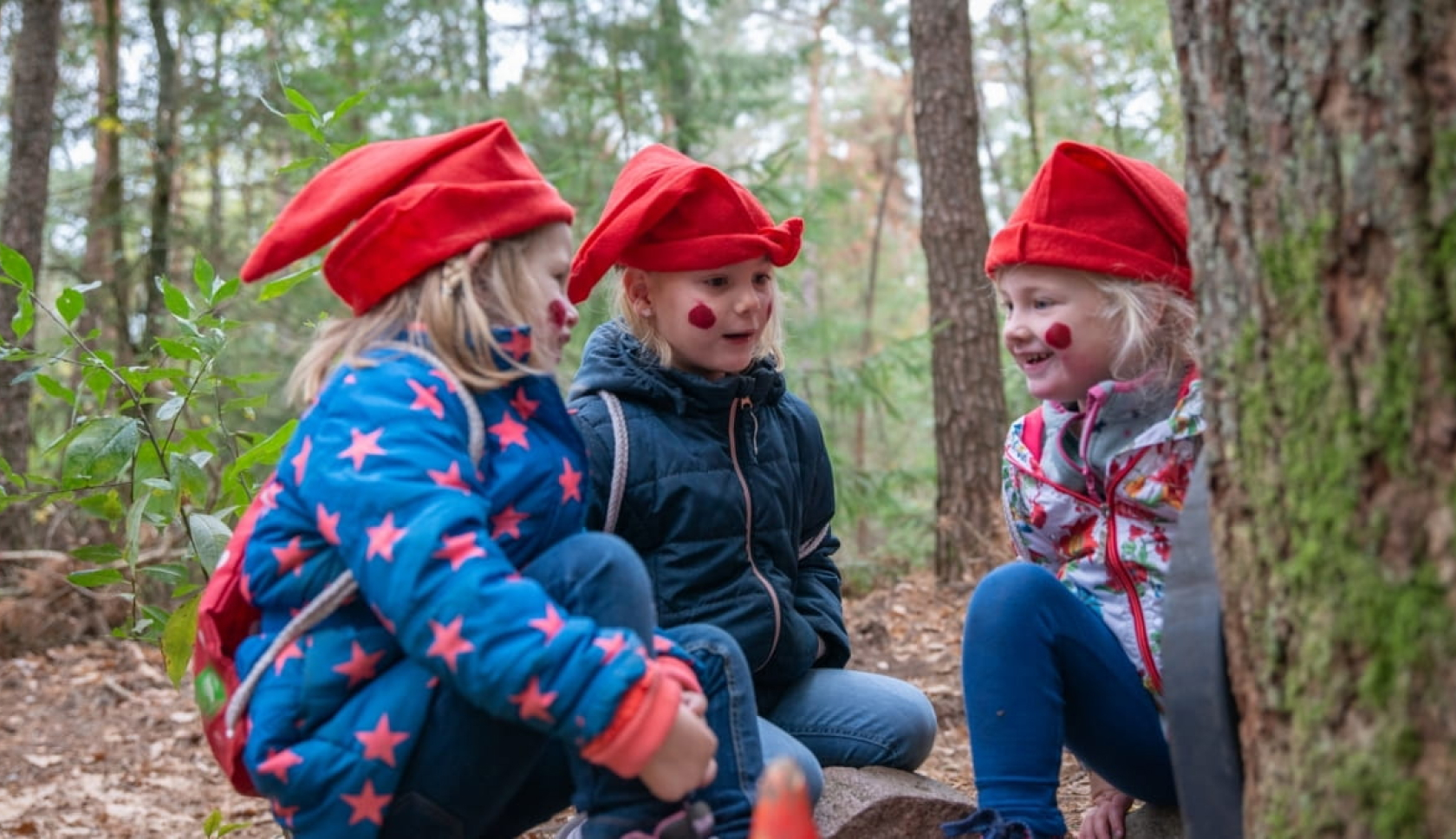 Kinderen met rode kaboutermutsen spelen samen in het bos op een kabouterpad