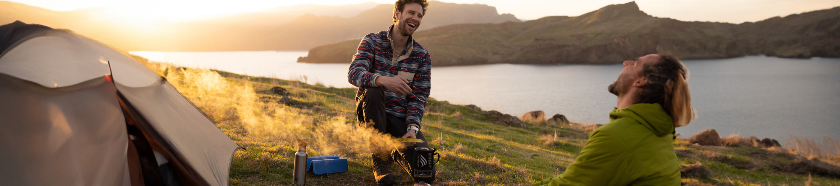 twee kampeerders lachen terwijl ze koken in bergachtig landschap
