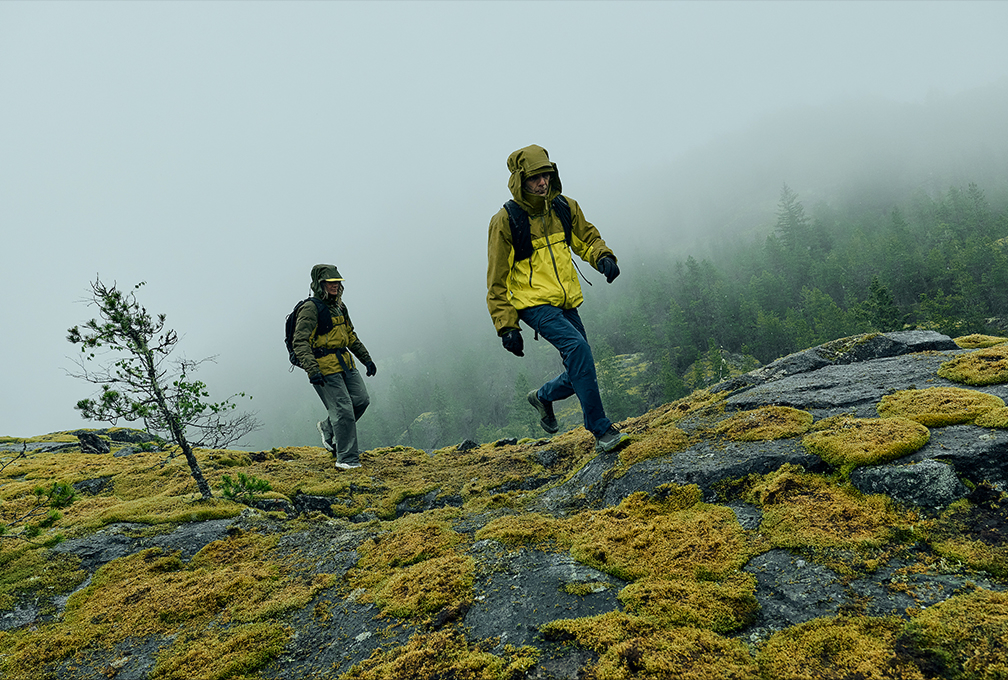 man en vrouw wandelen over een mossige berg met mistige bossen achter zich