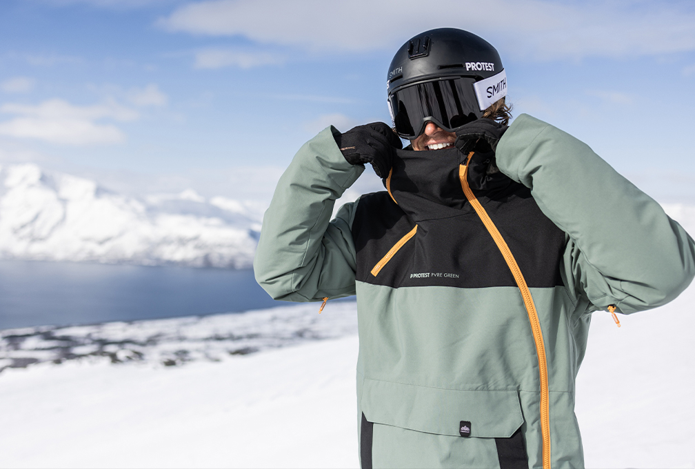 man met skihelm en skibrel op staat in de sneeuw en trekt de kraag van zijn sweater omhoog
