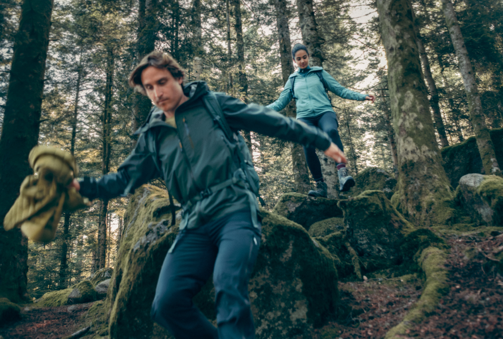 Twee wandelaars in een bos dragen Ayacucho-outdoorkleding tijdens een wandeling over rotsachtig terrein.
