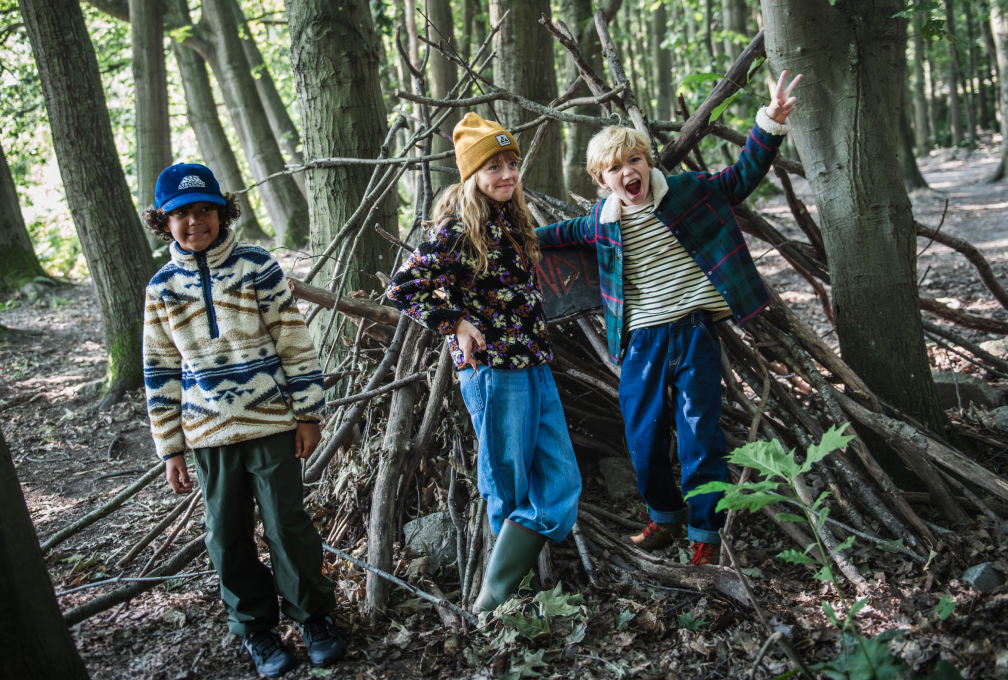 Drie kinderen in kleurrijke Ayacucho-outdoorkleding spelen samen in een bos.