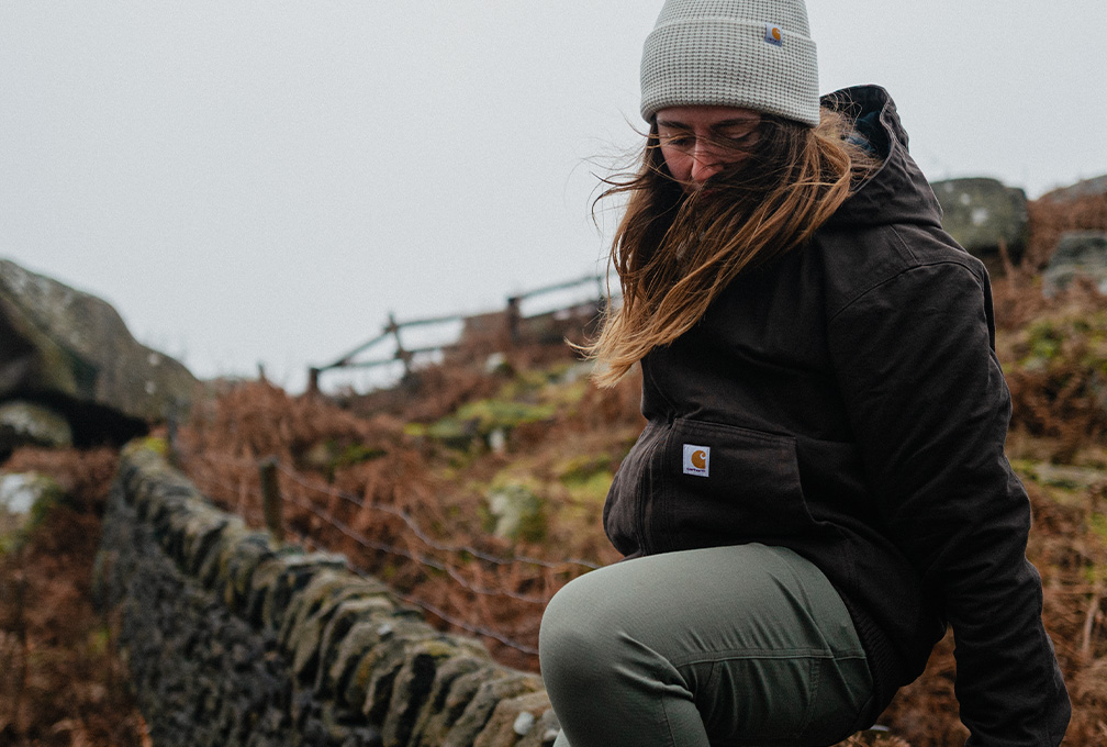 Vrouw in een zwarte Carhartt jas en grijze muts in de natuur