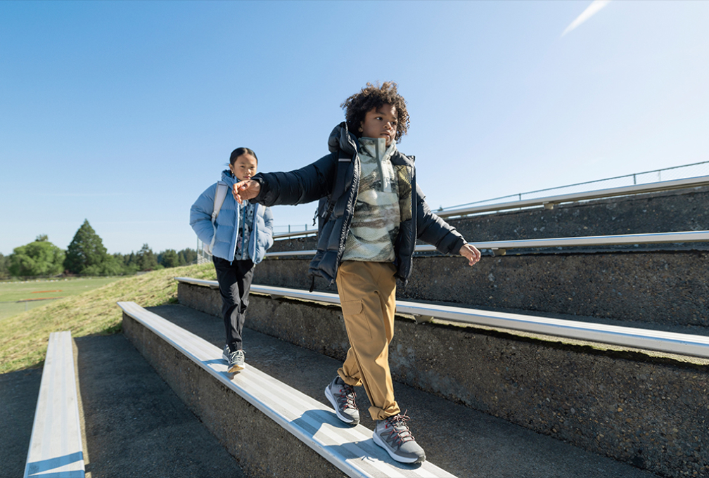 Twee kinderen in Columbia-outdoorkleding lopen over trappen in een buitenomgeving.
