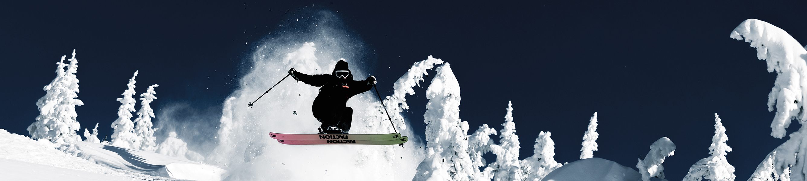 Skiër in Columbia-skikleding maakt een sprong door diepe sneeuw tussen besneeuwde bomen.
