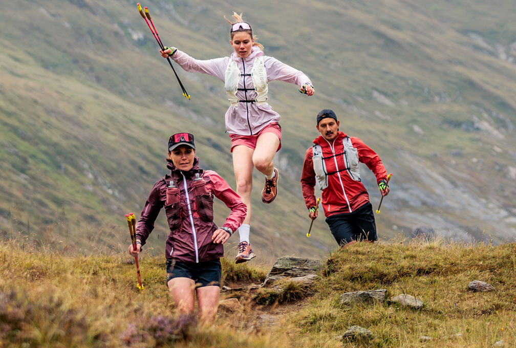 Drie trailrunners met LOWA-trailschoenen rennen door een bergachtig landschap.