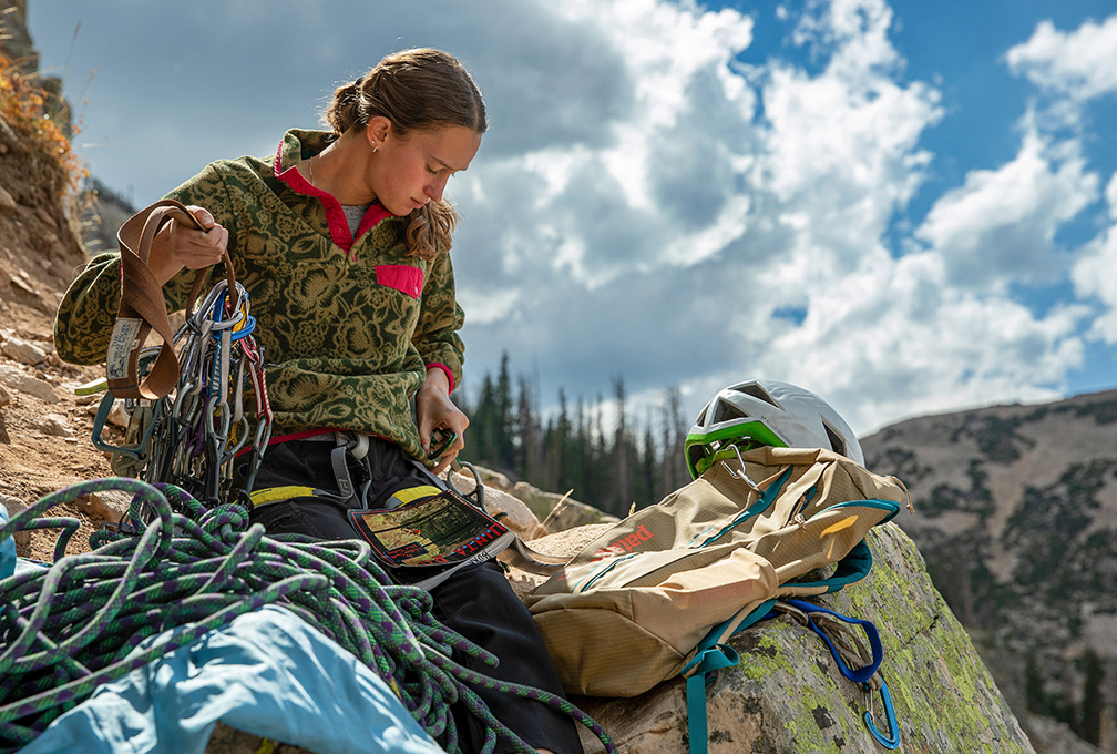 Klimmer in Patagonia-outdoorkleding sorteert klimuitrusting en touwen op een rots in de bergen.