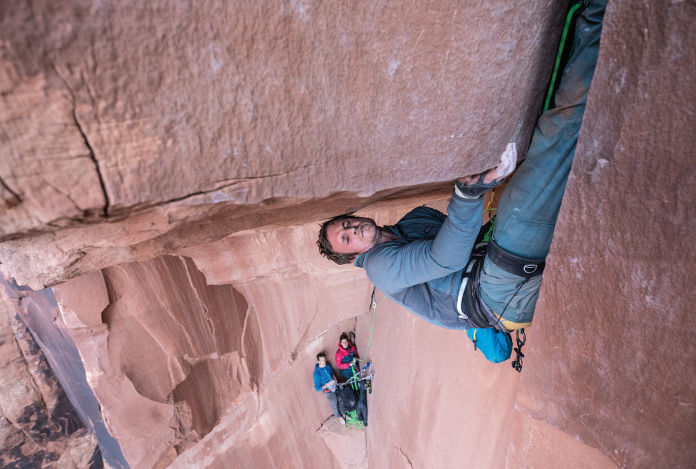 man klimt een moeilijke route terwijl twee mede-klimmers meekijken